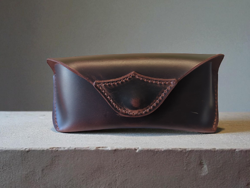 Brown leather eyeglass case with decorative stitching on a gray surface