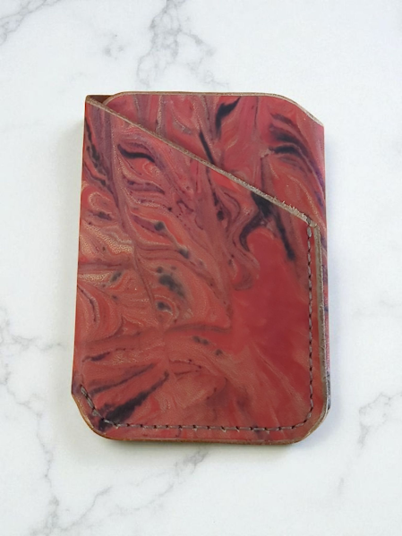Red marbled leather wallet with intricate patterns on a white marble background
