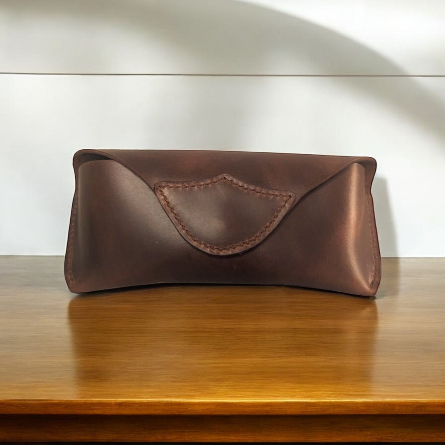 A dark brown leather eyeglass case with a magnetic closure, displayed on a wooden surface.